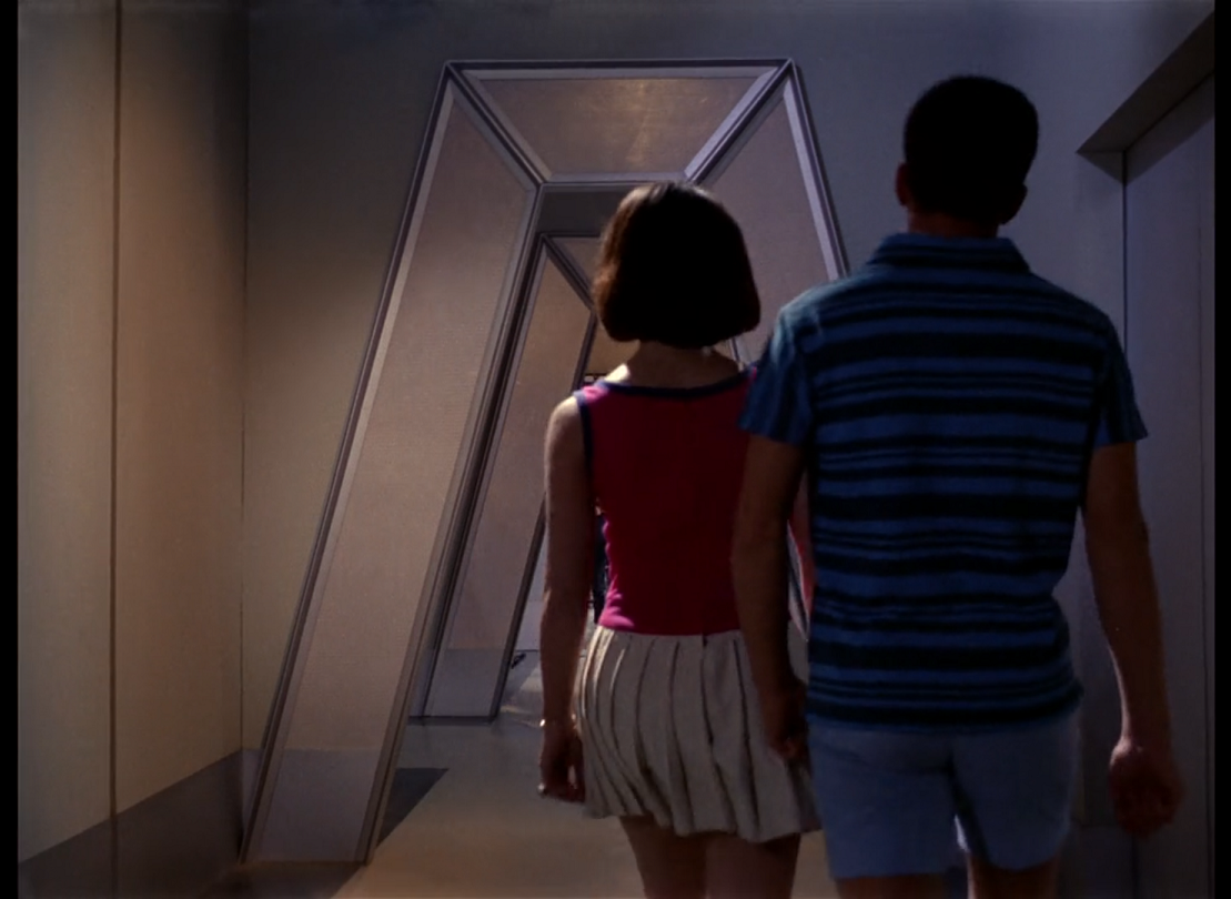 A man and a woman, seen from behind, walking through the Enterprise corridors. The woman is wearing a pink sleeveless shirt with a white pleated skirt, and the man is wearing a blue and black striped t-shirt with blue shorts.