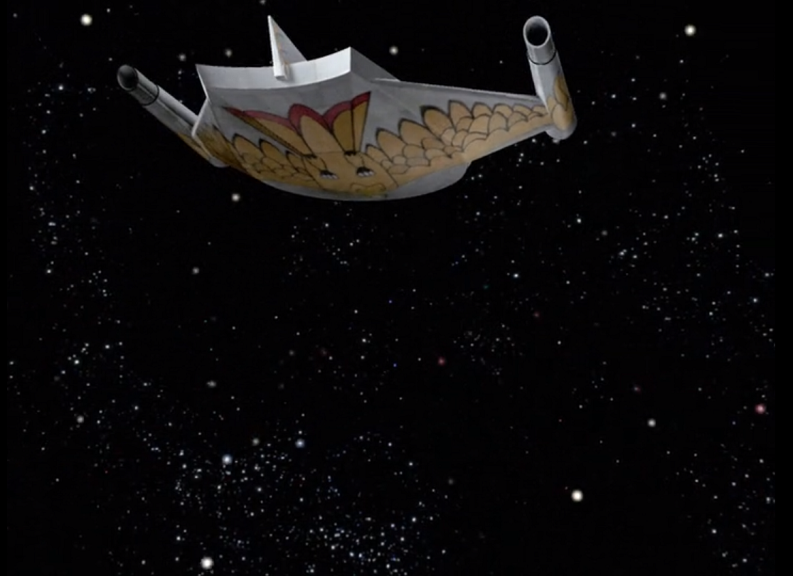 The Romulan ship flying through space. It is a mostly oval shape with a top fin and two triangular wings. The underside of the ship is painted with a stylized yellow and red bird in flight.