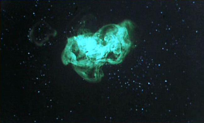A swirl of bright blue-green vapor glowing in the middle, in the midst of a starfield.