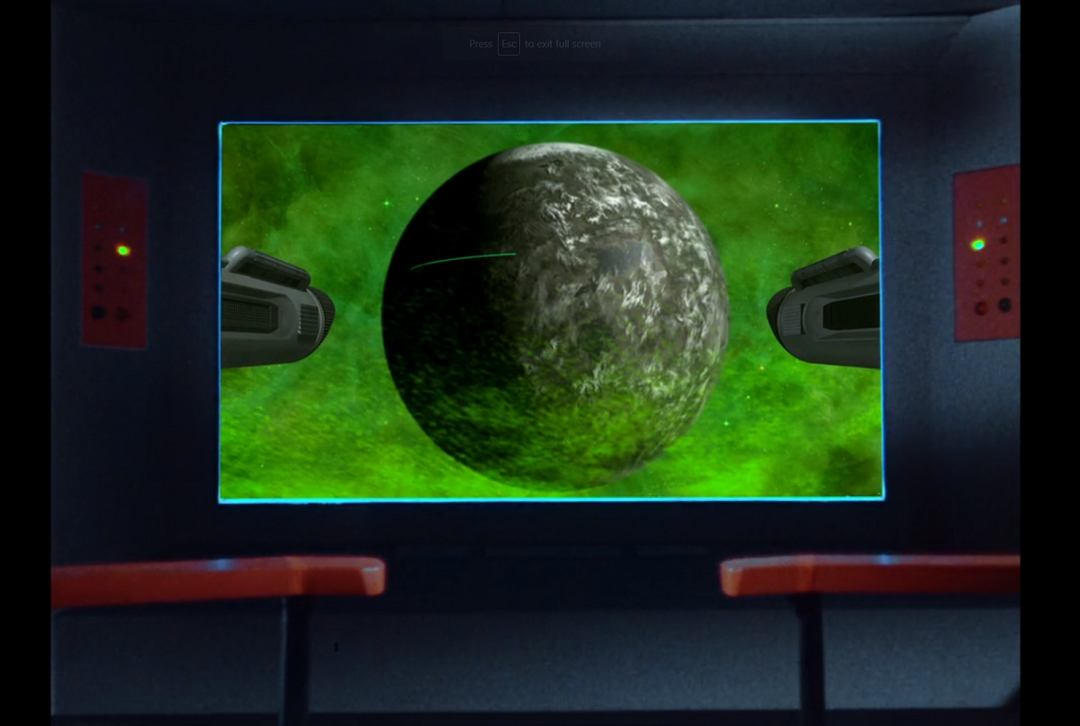 The viewscreen of the Enterprise, showing a rocky planet shrouded in green clouds, with a single bright green line trailing across it near the equator.